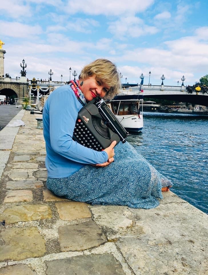 Kelye sitting beside the River Seine in Paris with one of her favorite typewriters.